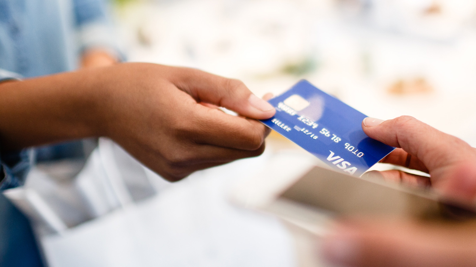 hand-card-chip-1600x900 Woman handing Visa card to clerk for purchase.