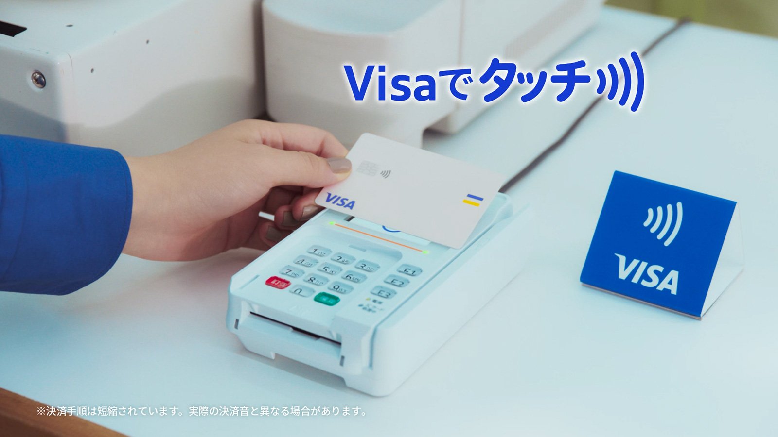 Visaカードをレジのリーダーに掲げ、タッチ決済とはどのように機能するかを表す手の画像